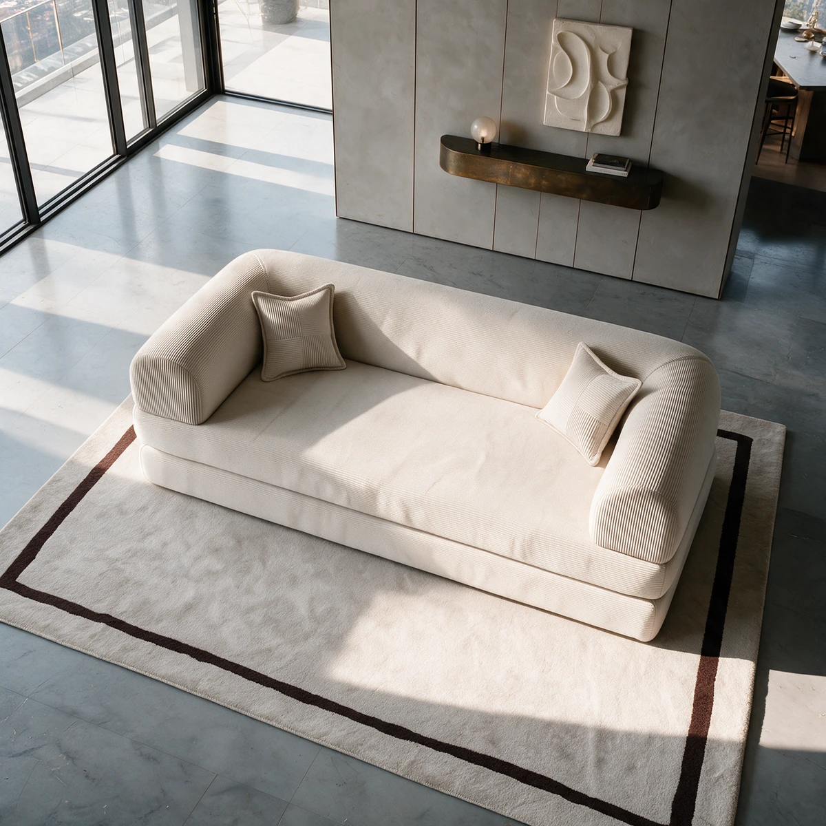 The Snoozo sofa bed in ecru fine corduroy seen from above, with two cushions, on a cream rug beside tall windows, with sunlight falling across the floor
